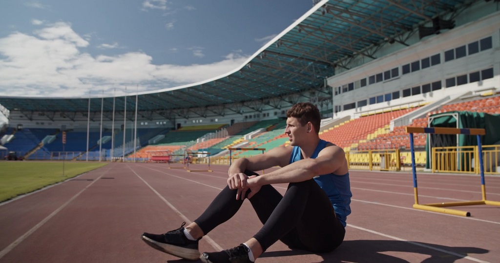 Atletičar sedi na stazi posle treninga i odmara