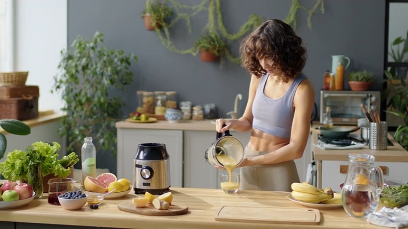 Žena u sportskoj odeći priprema zdrav smoothie u kuhinji